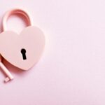 Aesthetic photo of a heart-shaped pink padlock with a matching key on a pink background, perfect for love themes.