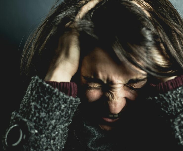 Close-up of a woman in distress with eyes closed and hands in hair, expressing anxiety.