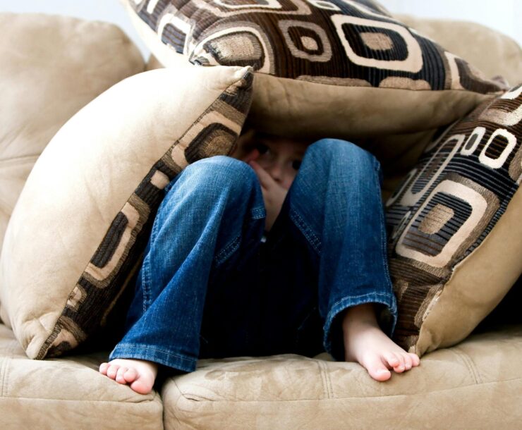 A child crouched under cushions on a couch, conveying a sense of playfulness or fear.