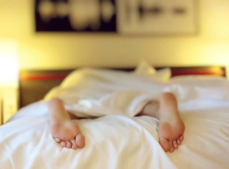 A person relaxing on a bed with feet under white sheets, conveying serenity.