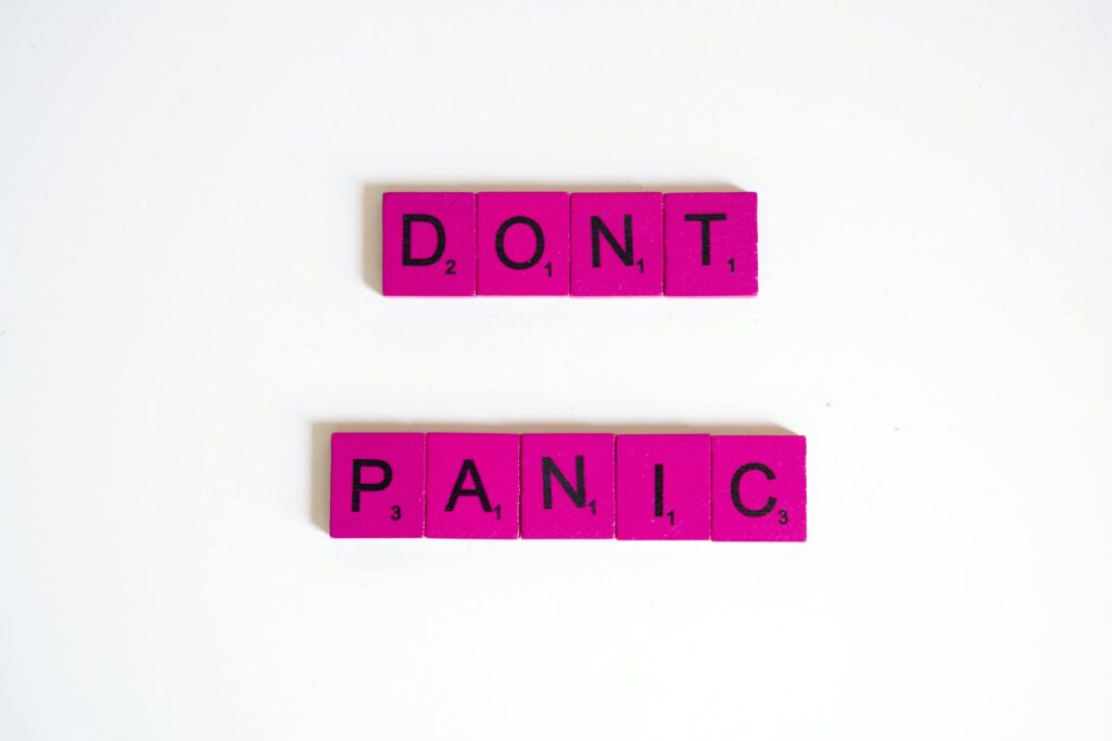 Pink Scrabble tiles spell out 'Don't Panic' on a white background.