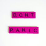Pink Scrabble tiles spell out 'Don't Panic' on a white background.