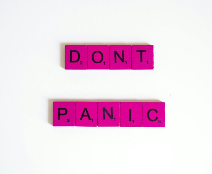 Pink Scrabble tiles spell out 'Don't Panic' on a white background.