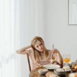 A teenage girl sits dissatisfied at breakfast with various food items on a wooden table.