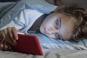Child lying in bed under a blanket, focused on a smartphone screen, displaying a bedtime routine.