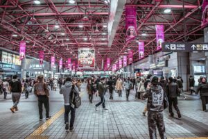 A bustling indoor train station filled with commuters and vibrant signage, showcasing urban life.