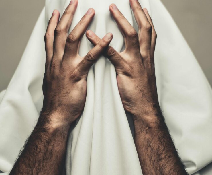 Person covered with white cloth, hands on head, expressing mystery and stress.