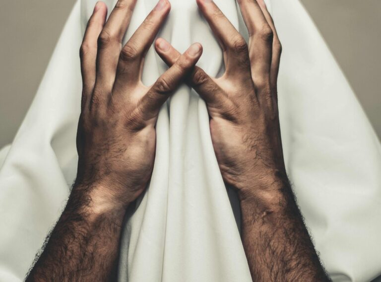 Person covered with white cloth, hands on head, expressing mystery and stress.