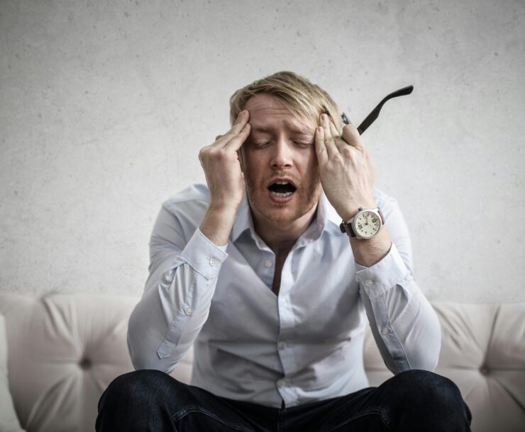 Stressed man sitting on couch, feeling overwhelmed and frustrated, expressing mental strain.