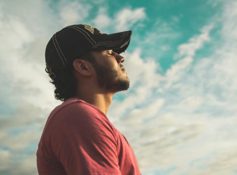 A man enjoys outdoor relaxation and mindfulness beneath a bright, cloudy sky, exuding calm and peace.