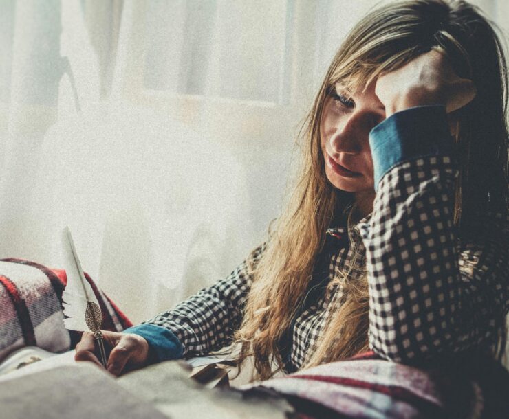 pexels-photo-1650209-1650209 A woman with a quill, deep in thought by a sunlit window, in a plaid shirt.