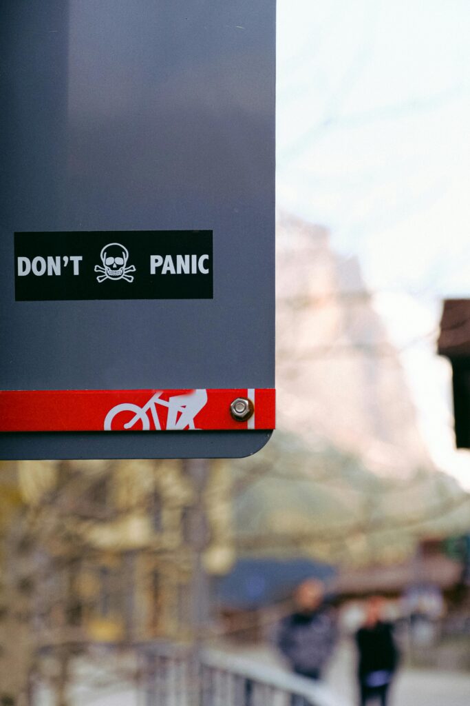 Street sign with 'Don't Panic' message featuring a skull, shot outdoors with blurred background.