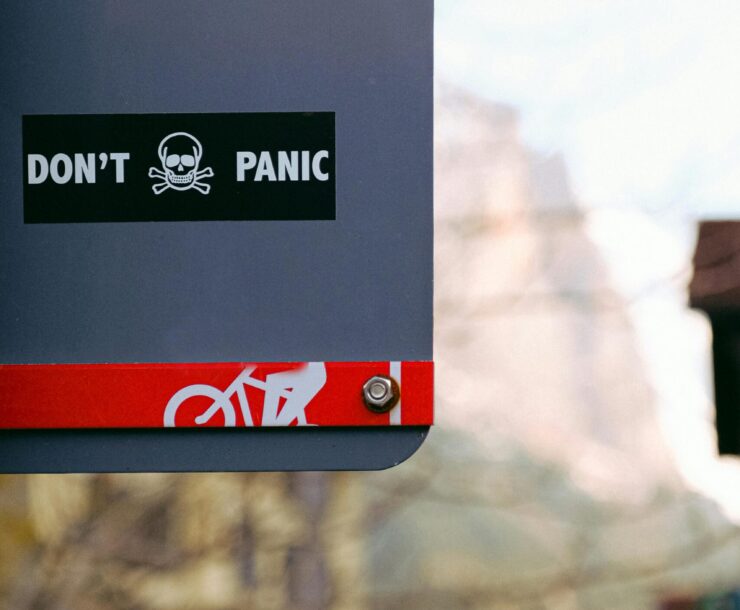 Street sign with 'Don't Panic' message featuring a skull, shot outdoors with blurred background.