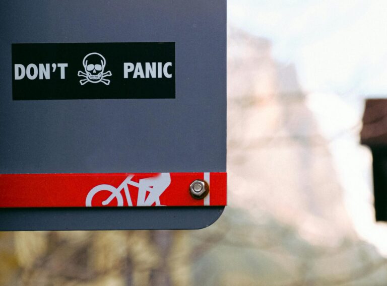pexels-photo-3962262-3962262 Street sign with 'Don't Panic' message featuring a skull, shot outdoors with blurred background.